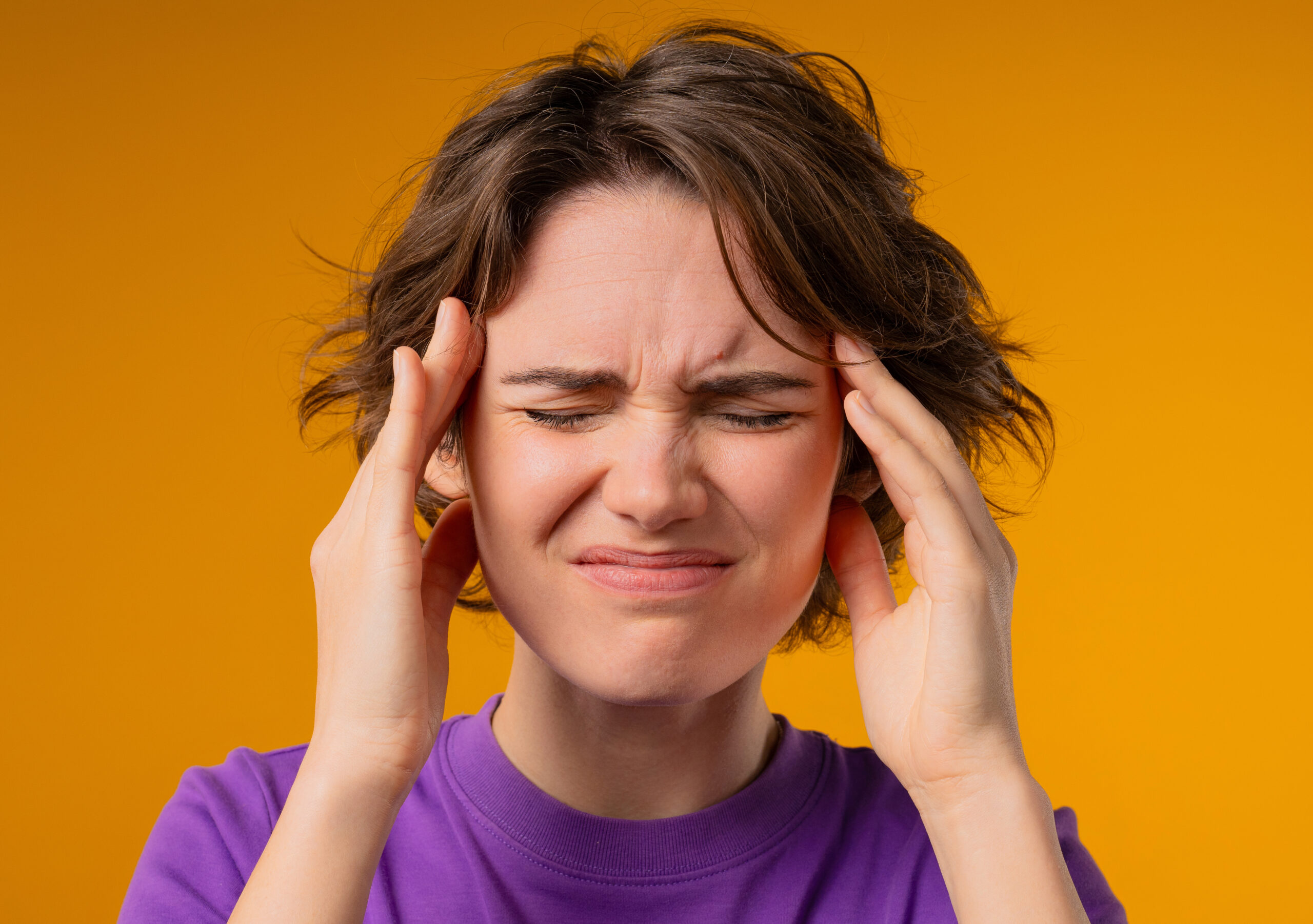 Portrait of beautiful suffering woman having headache, yellow studio portrait. Girl putting hands on head. Concept of migraine problems, medicine, illness, magnetic storms concept.